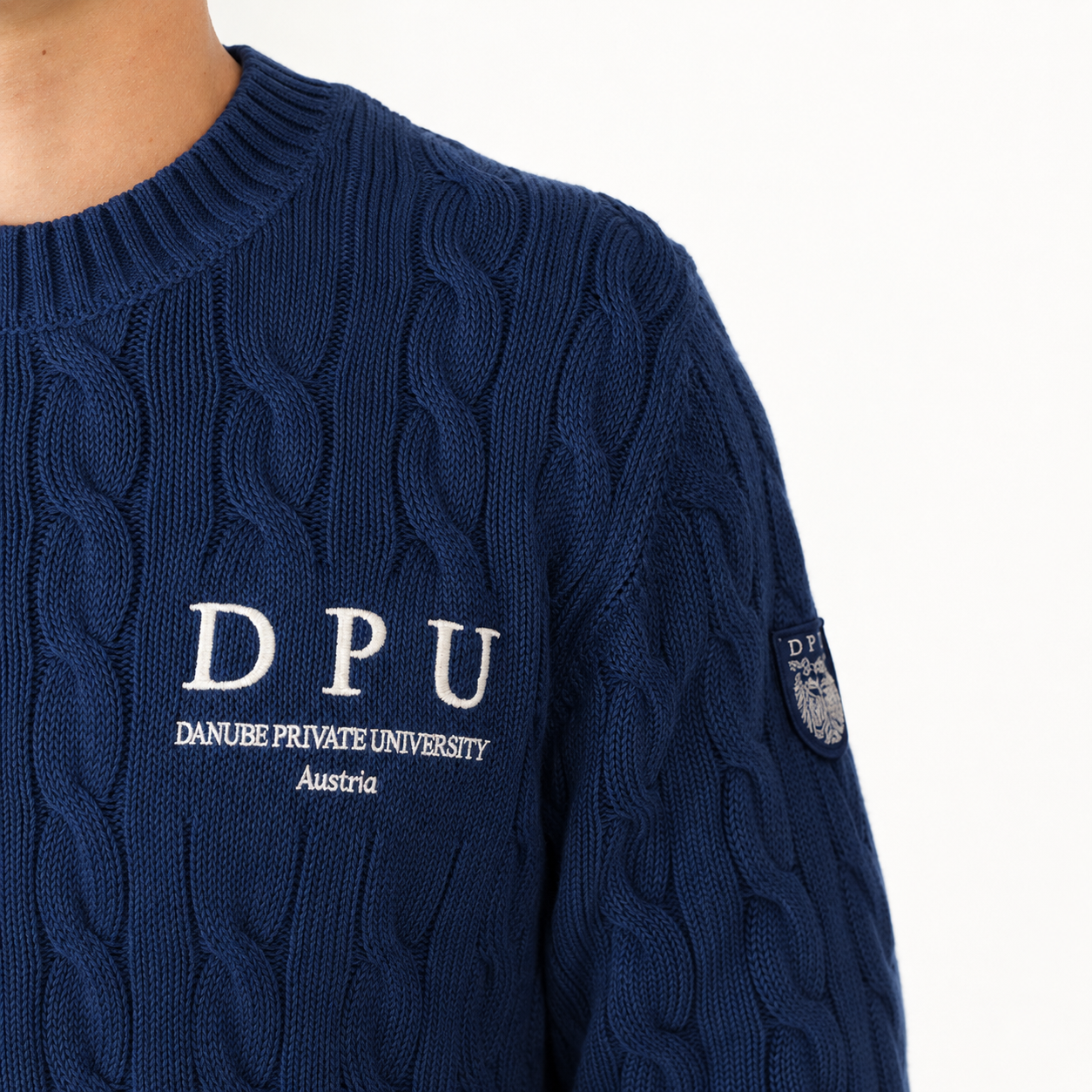 DPU Strickpullover in dunkelblau mit klassischem Zopfmuster, winterweißem DPU-Stick und aufgenähtem Wappen-Patch am Ärmel.