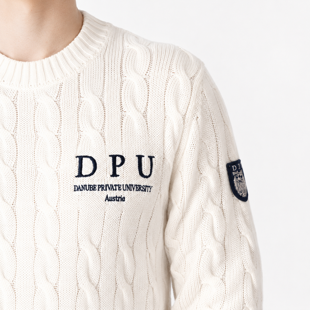 DPU Strickpullover in Winterweiß mit klassischem Zopfmuster, blauem DPU-Stick und aufgenähtem Wappen-Patch am linken Ärmel.