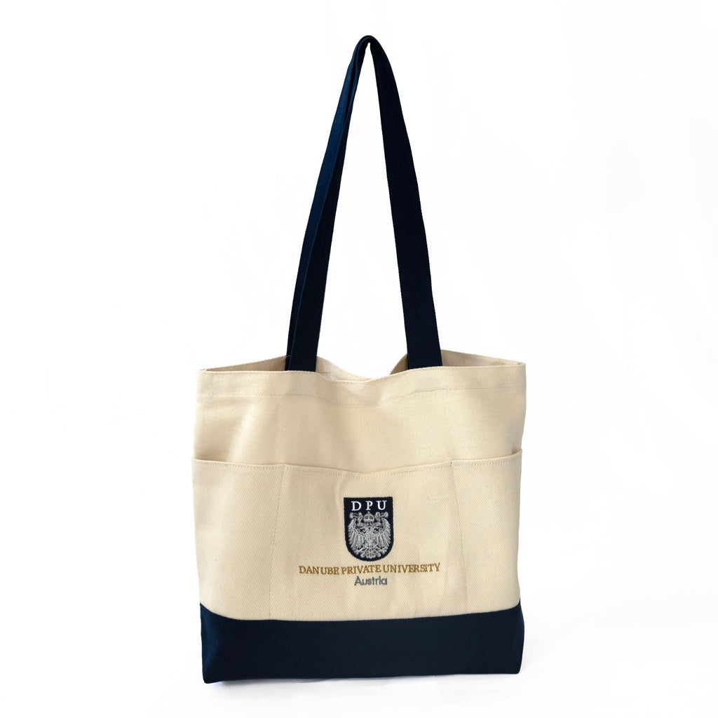 DPU Shopper aus 100 % Baumwolle in Winterweiß und Blau mit 3 Außentaschen und langen Tragegriffen. Mit DPU-Wappen und DPU-Schriftzug auf der Vorderseite sowie hochwertiger 320 gsm Qualität.