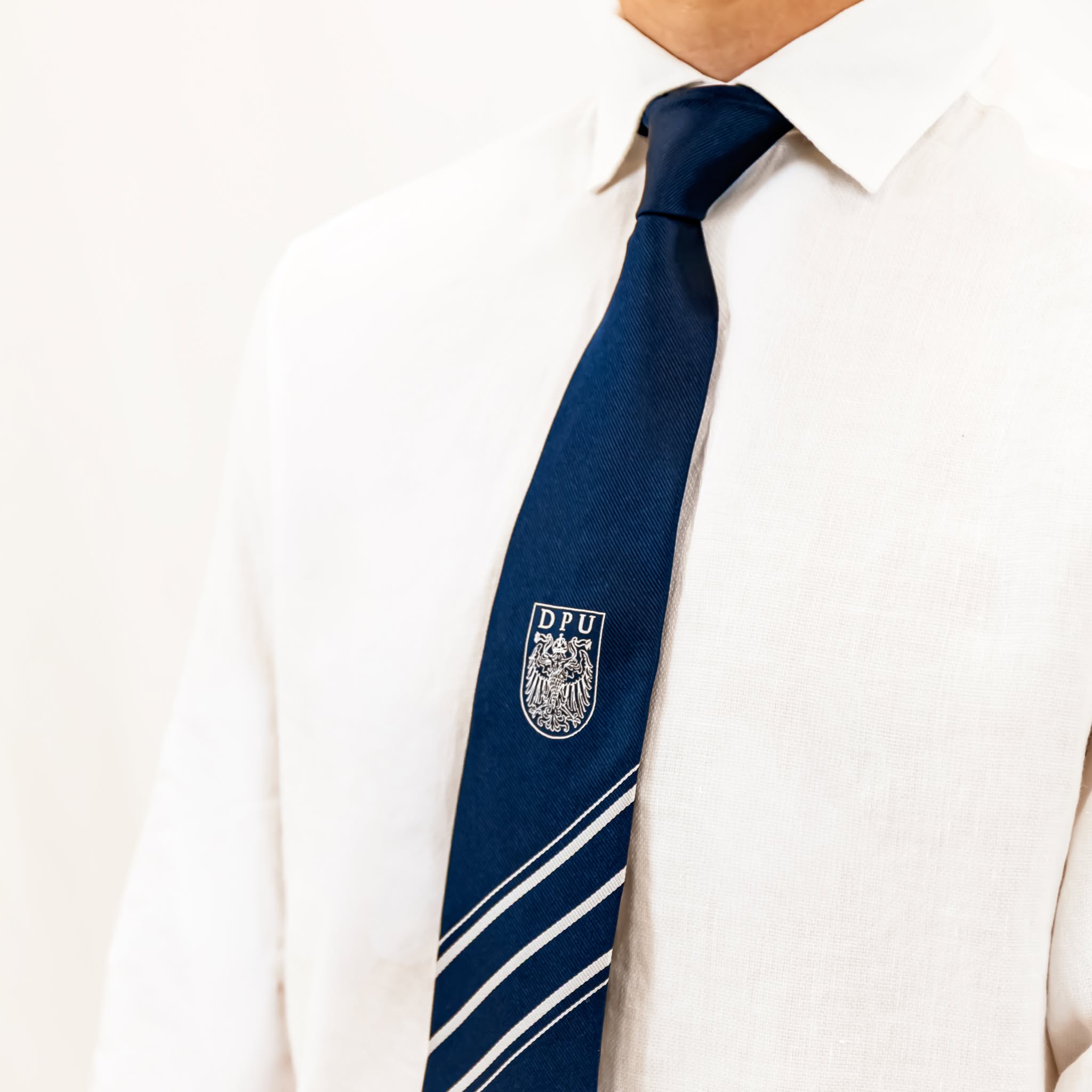 Dunkelblaue DPU-Krawatte mit weißen Streifen und eingearbeitetem DPU-Wappen, gefertigt in Italien.