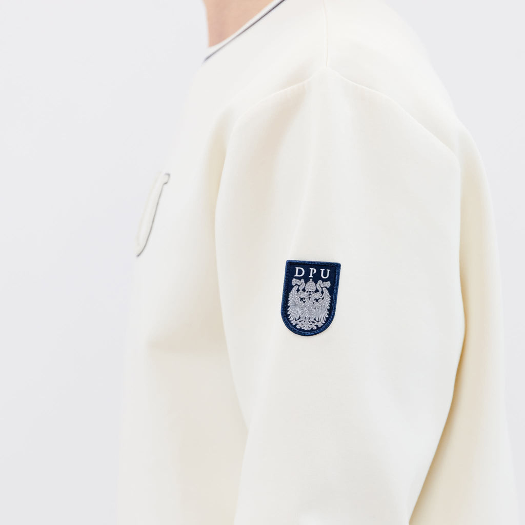 Detailaufnahme vom Ärmel des Winterweißen DPU-Sweatshirt mit Wappen-Patch am linken Ärmel.